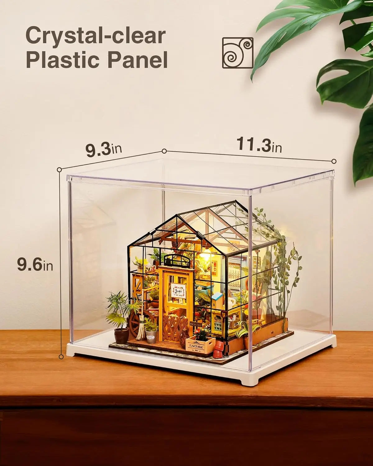 Clear acrylic display case containing a miniature greenhouse model on a wooden surface