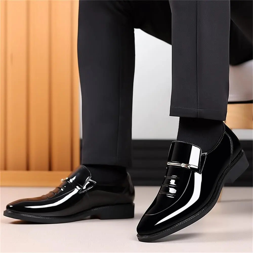 A man wearing black formal trousers and black socks, demonstrating a pair of black patent leather loafers.