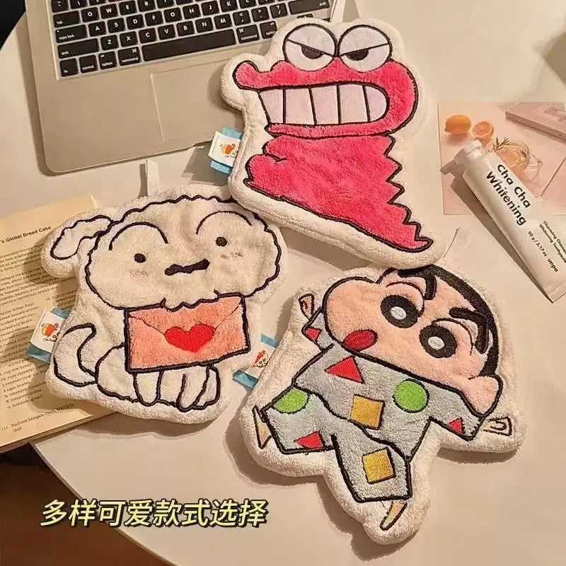A collection of three cartoon-themed hanging hand towels displayed on a desk with a laptop and a tube of toothpaste.