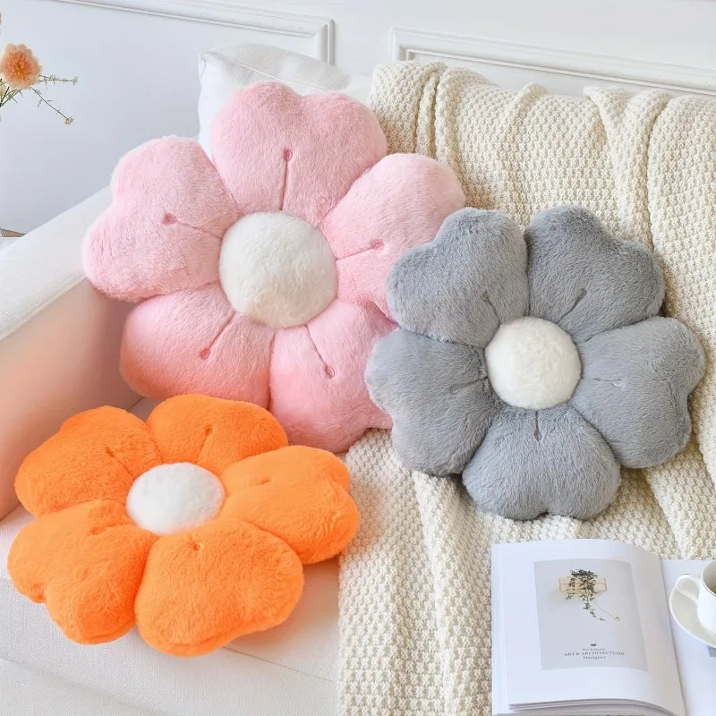 A pink plush flower pillow and a gray plush flower pillow on a beige sofa.