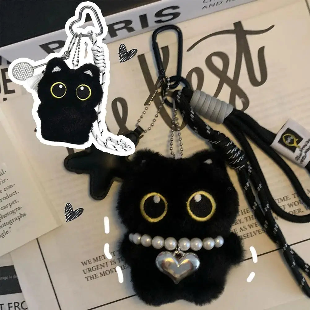 Black cat plush keychain with a pearl and heart necklace against a newspaper background.