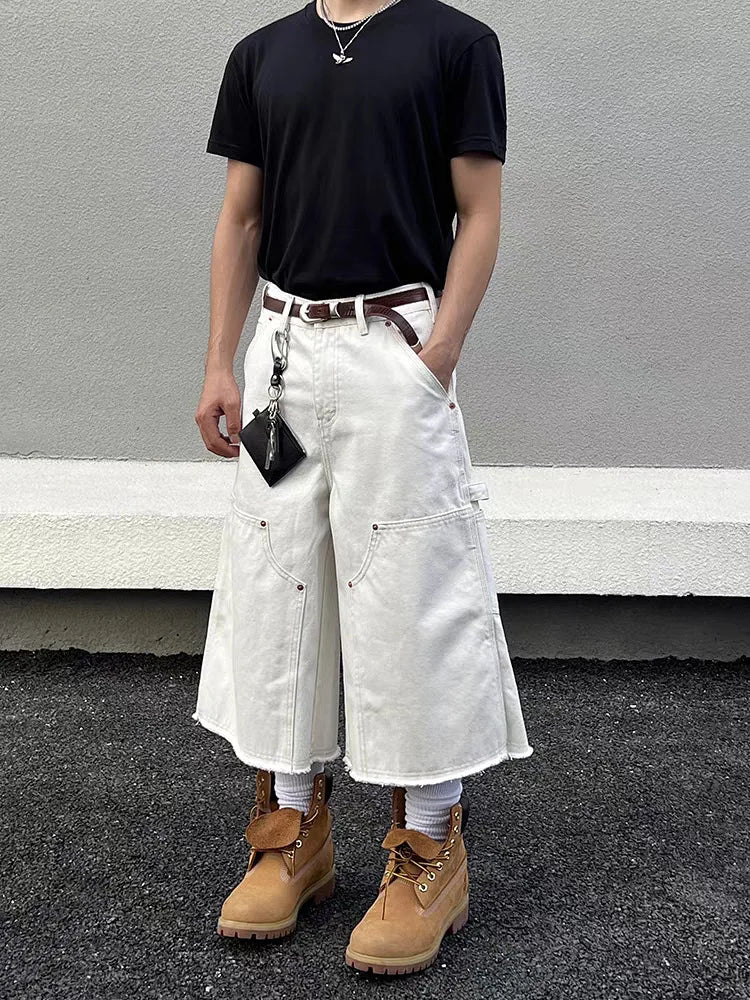 Men's white wide-leg carpenter denim jorts with frayed hem, black t-shirt, and tan work boots.