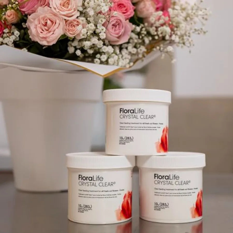 Three containers of flower food powder stacked in front of a bouquet of pink roses