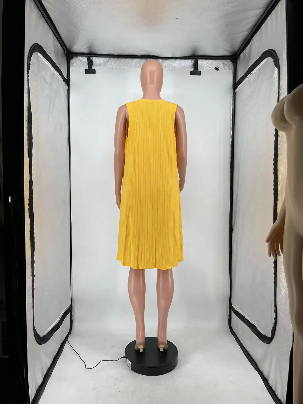 The back view of a long sleeveless yellow ribbed cardigan displayed on a mannequin.