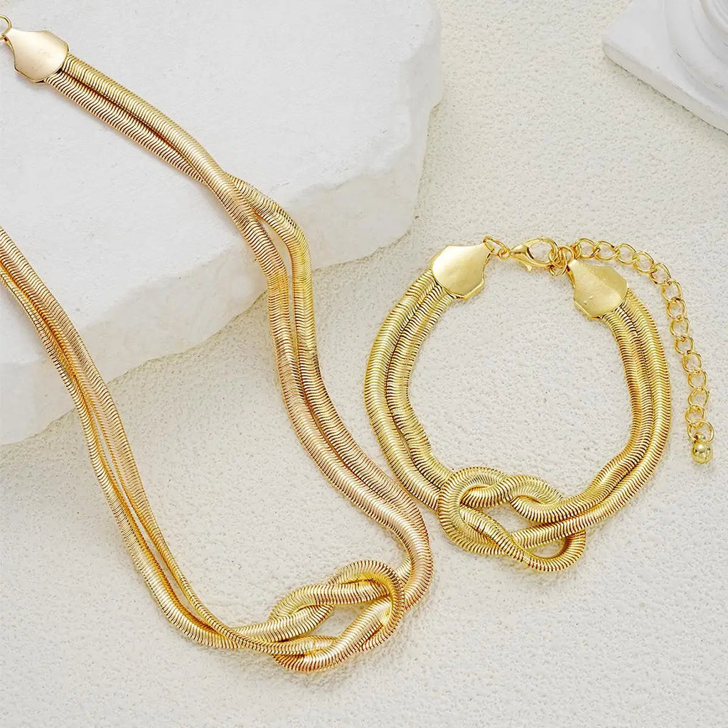 Gold double layer knot necklace and matching bracelet on a white textured surface