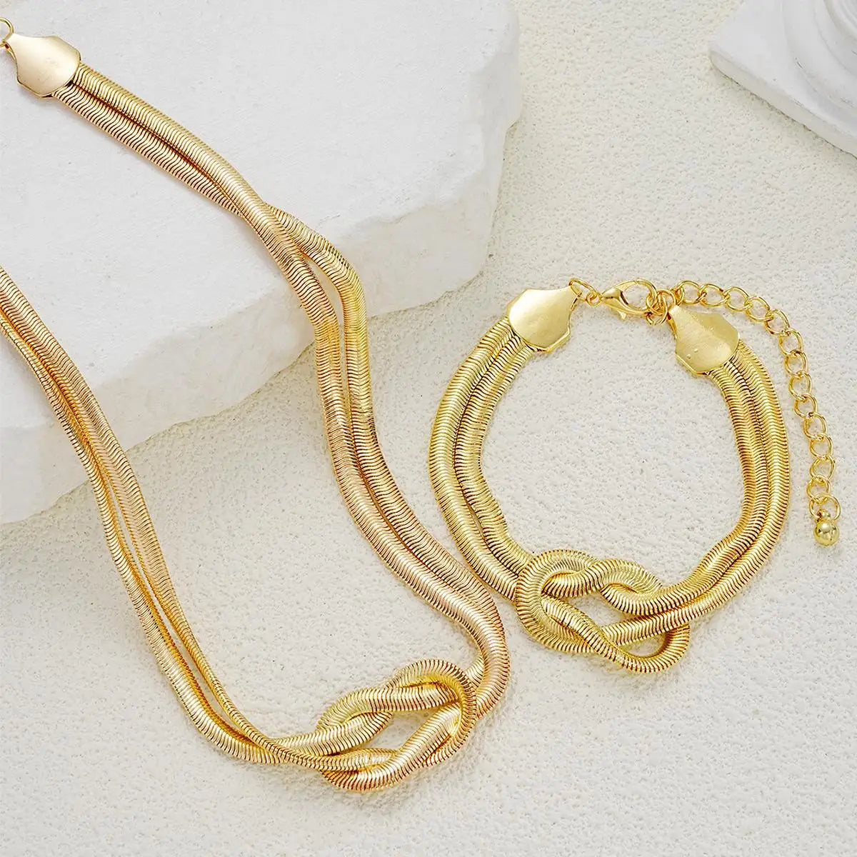 Gold double layer knot necklace and matching bracelet on a white textured surface