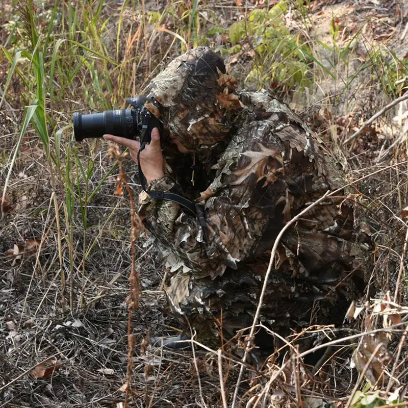 Hunter in 3D leaf woodland ghillie suit holding a camera in a forest