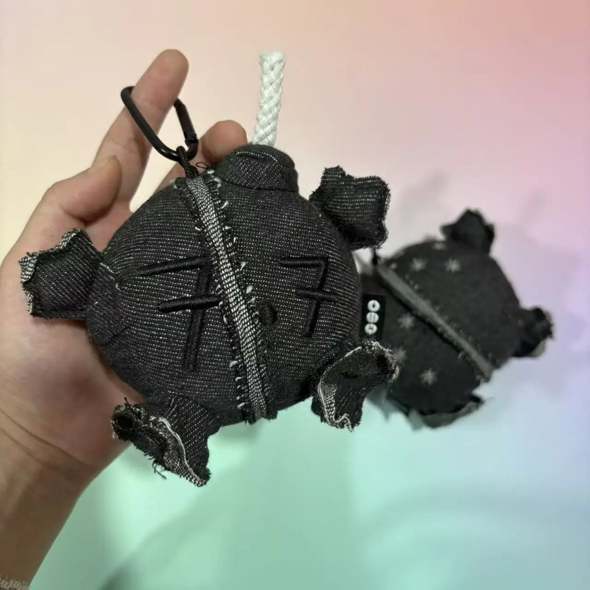 Hand holding a grey denim plush ball doll pendant with a white rope wick