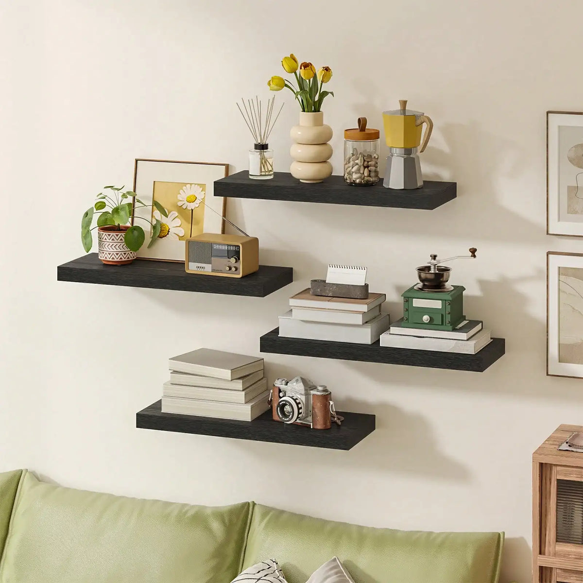 Four black floating shelves arranged on a living room wall, holding decor like potted plants, books, and a camera