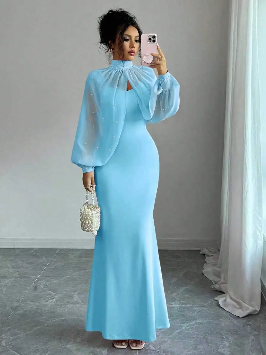 A woman wearing a light blue floor-length mermaid gown with a beaded sheer cape-style top.