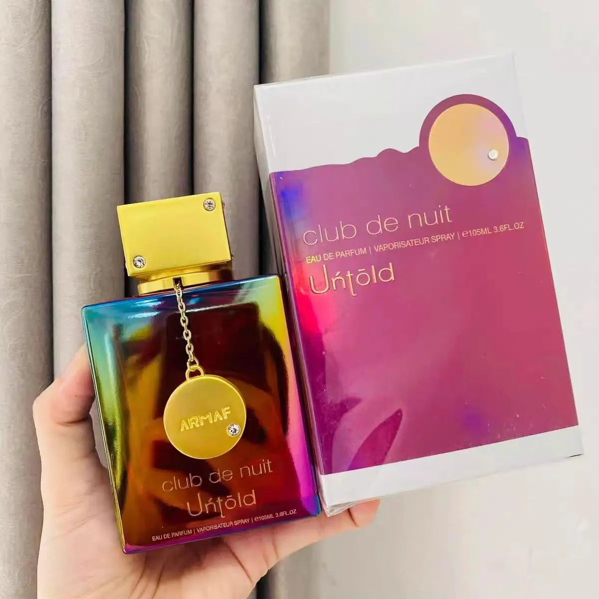 Gradient perfume bottle with gold cap held in hand with a box on the side