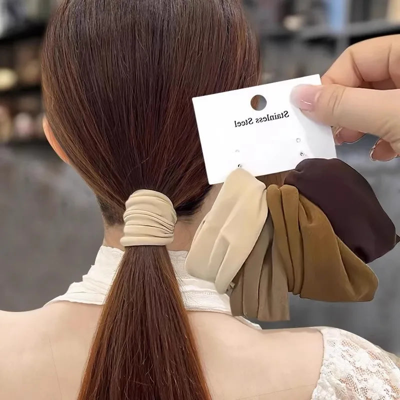 A woman's hair in a ponytail with a tan stretchy hair tie, showing multiple colors of hair scrunchies held in hand
