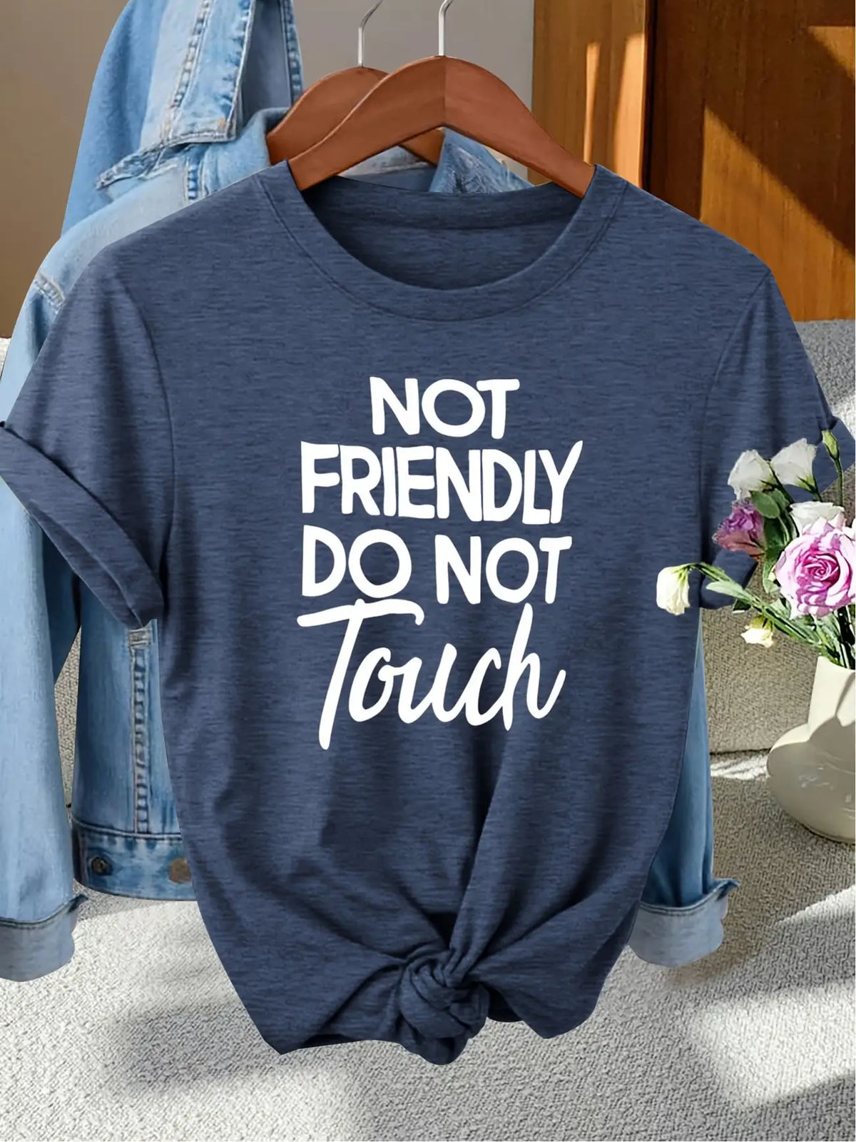 Navy blue short sleeve T-shirt with white text printed on the front, hanging on a wooden hanger with a denim jacket
