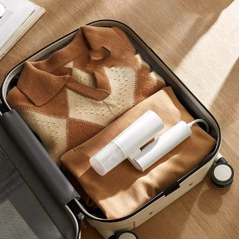 Portable white garment steamer inside a suitcase with folded clothing.