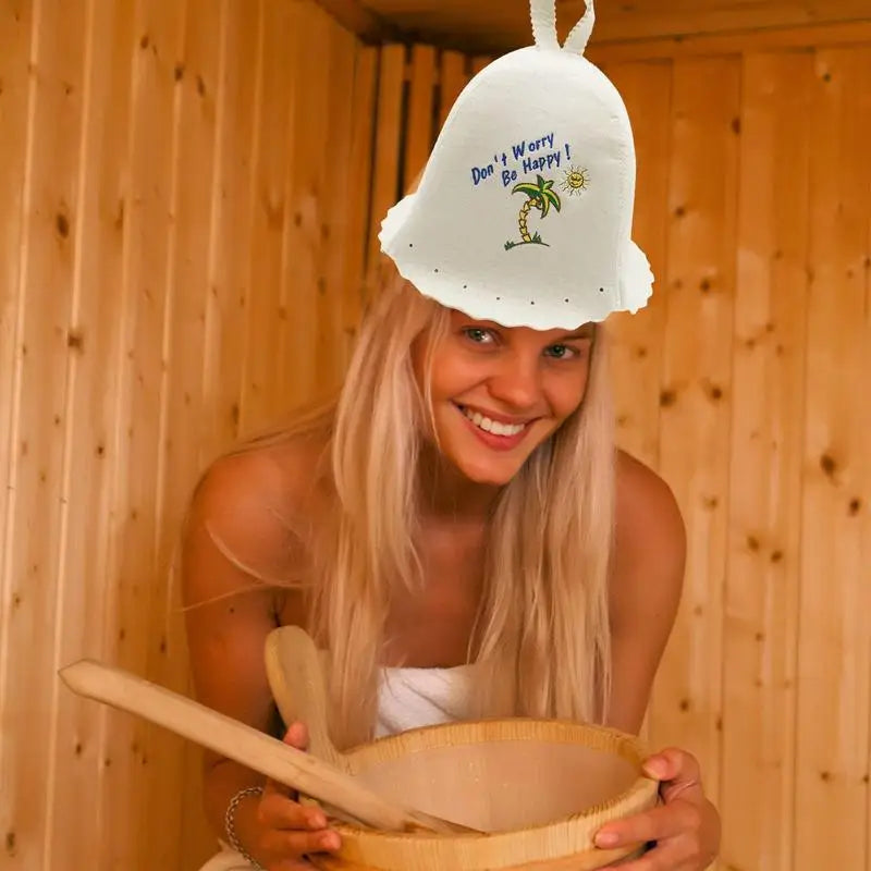 A woman wearing a white felt sauna hat with palm tree embroidery in a wooden sauna.