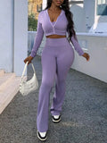 A woman wearing a purple long-sleeve zip-up top and matching flared trousers, carrying a white shoulder bag.