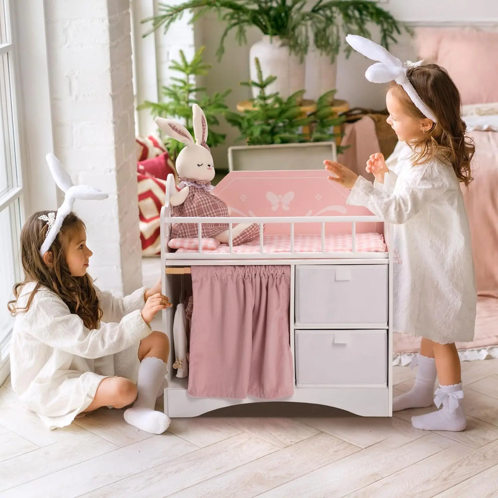 Two young girls playing with a white and pink wooden doll crib in a nursery
