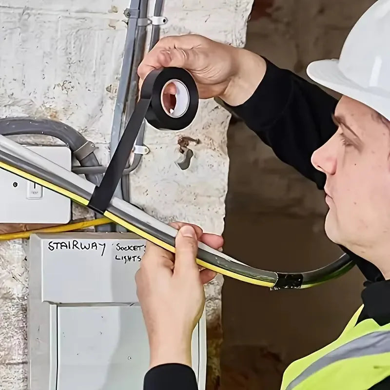 An electrician wearing a helmet using black electrical tape on wiring inside a building.