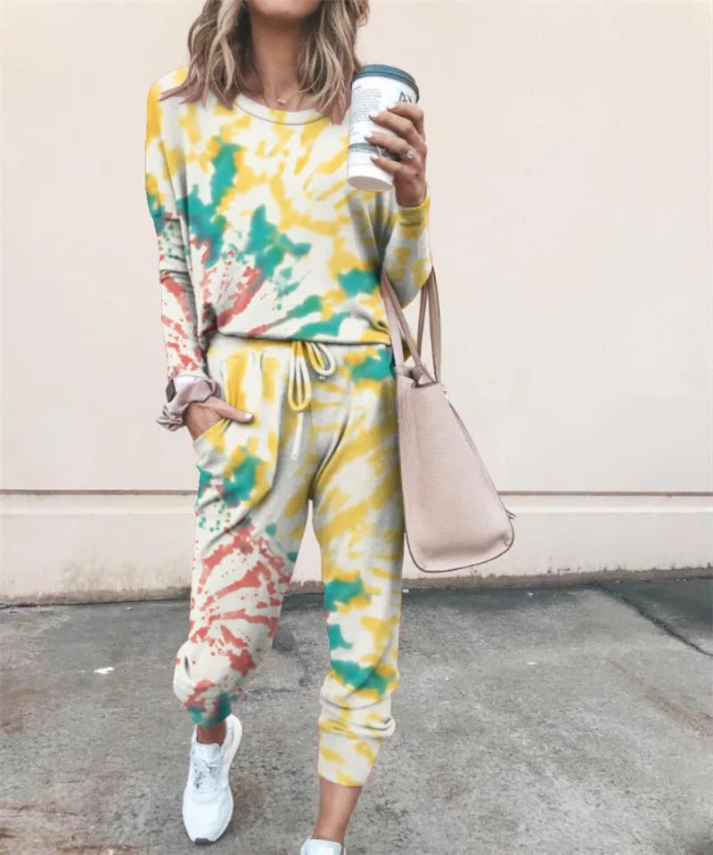 A woman wearing a yellow and green tie-dye long-sleeve top and jogger pants set, holding a takeaway coffee cup.