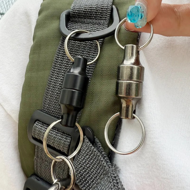 A hand holding two magnetic keychain connectors with metal rings.