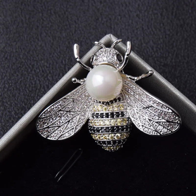 Silver-toned bee brooch with a pearl body, rhinestone wings, and black and yellow crystal stripes.