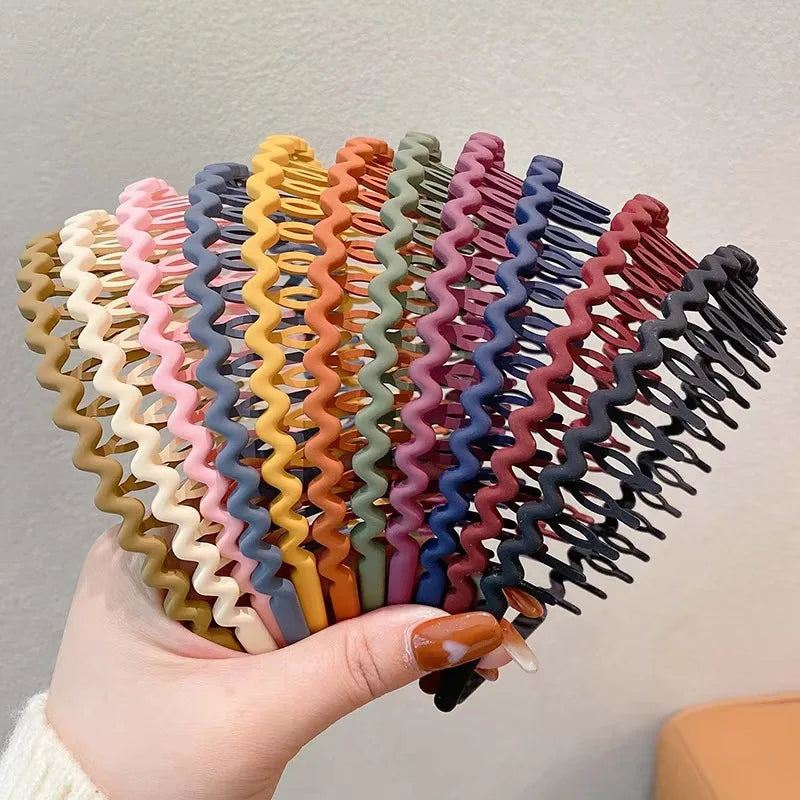 A hand holding a multi-colored collection of wavy, toothed plastic headbands