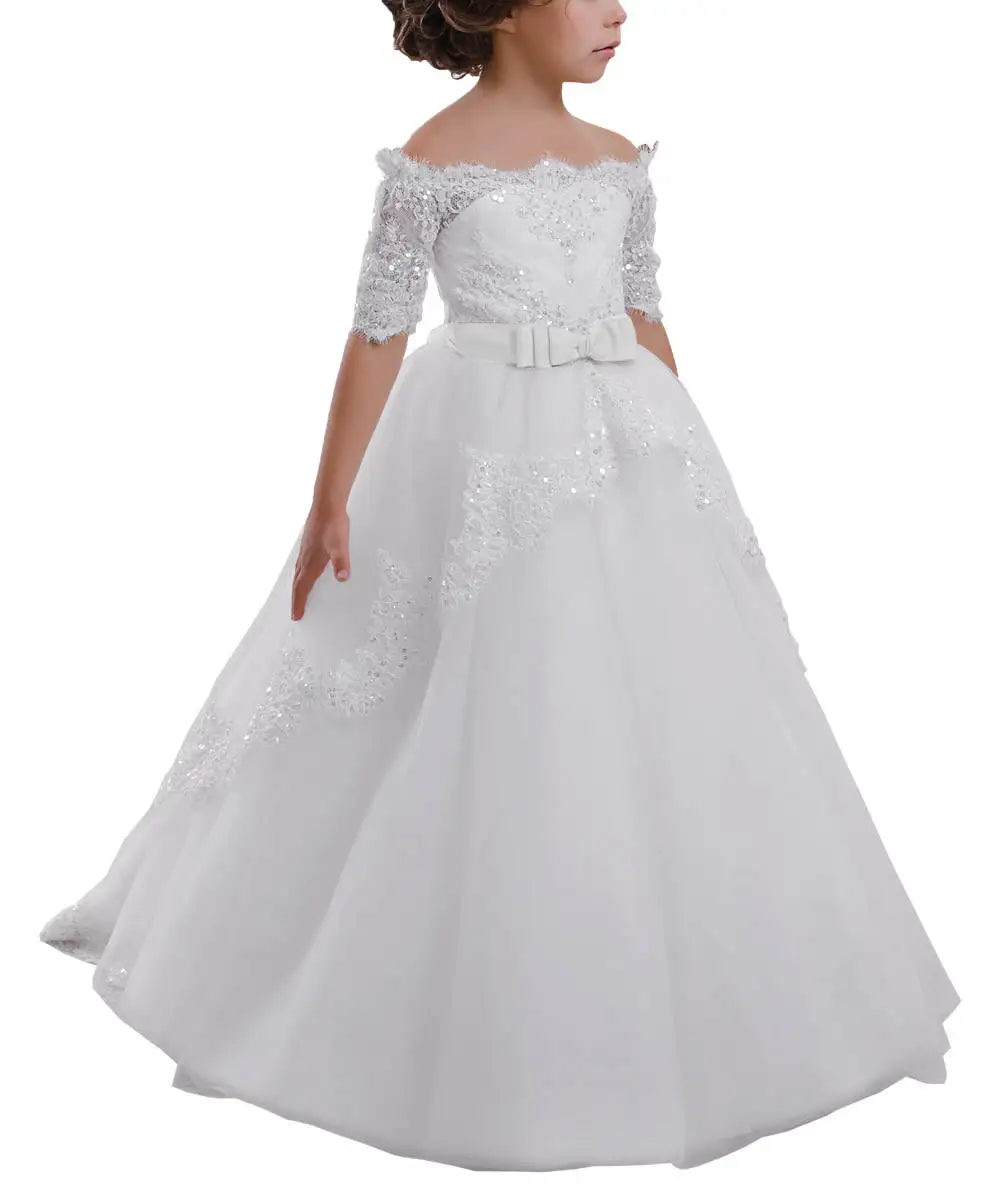 White off-shoulder flower girl dress with lace, sequins, tulle skirt, and a bow at the waist on a white background.