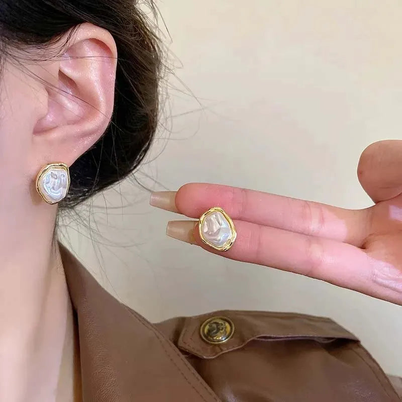 Person wearing gold-rimmed irregular pearl earrings