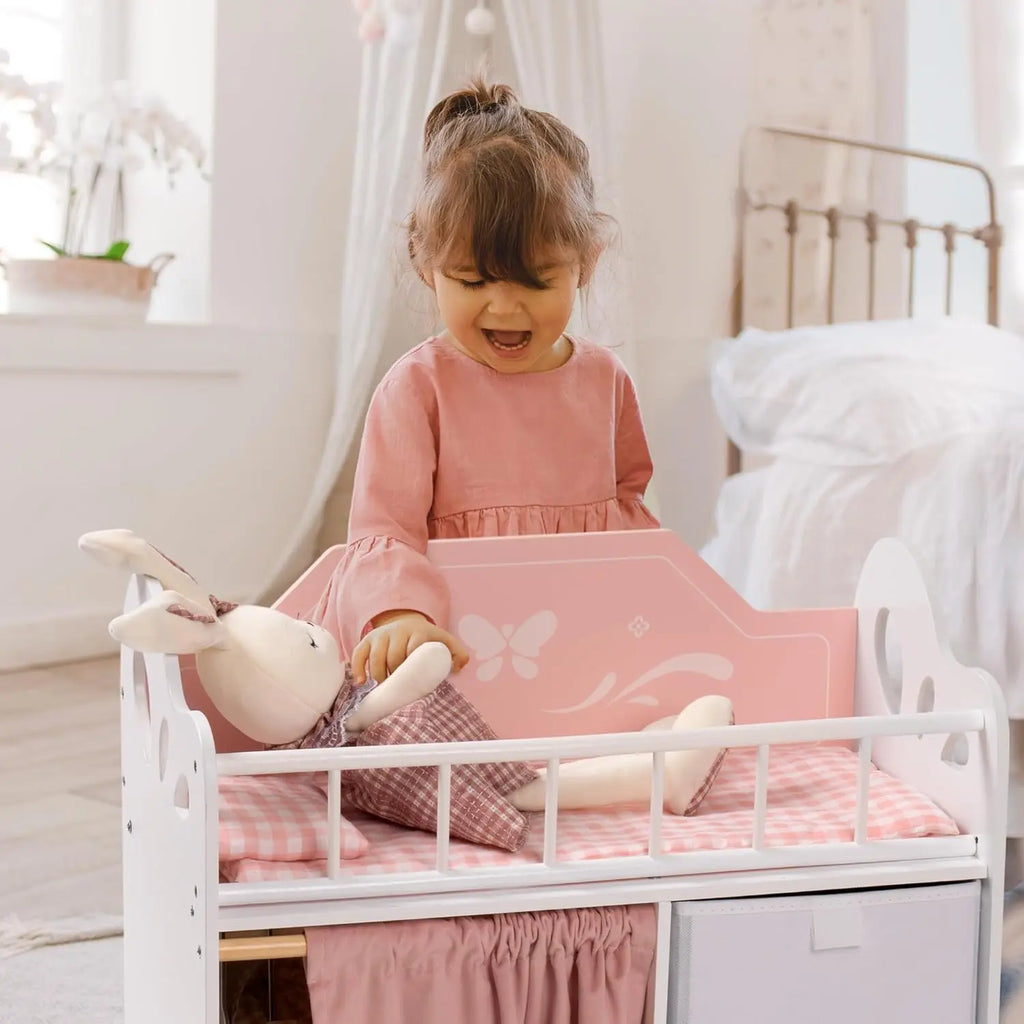 A young girl playing with a doll in a white and pink wooden baby doll crib