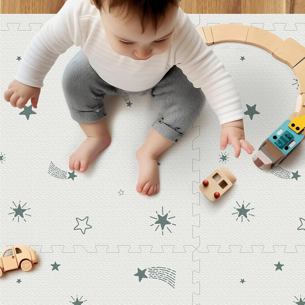 Baby sitting on a white foam play mat with green star patterns, playing with wooden toy vehicles.