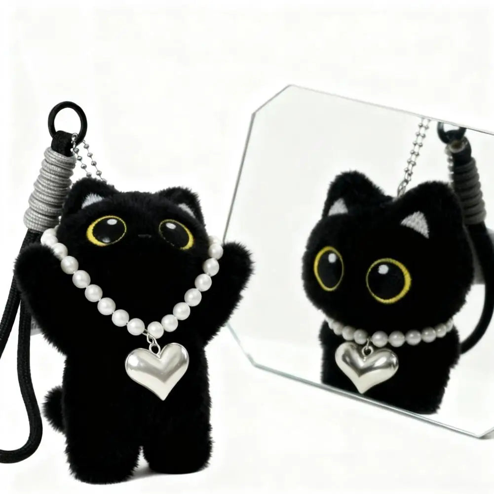 Black cat plush keychain with a pearl and heart necklace reflected in a small mirror.