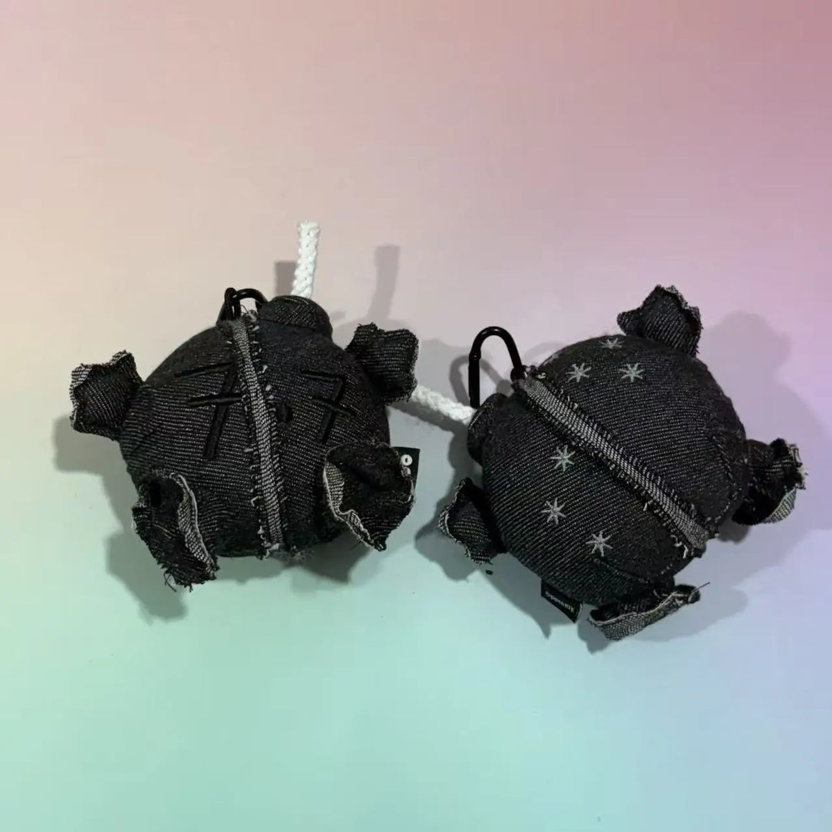 Two grey denim plush ball doll pendants with white rope wicks and carabiner clips
