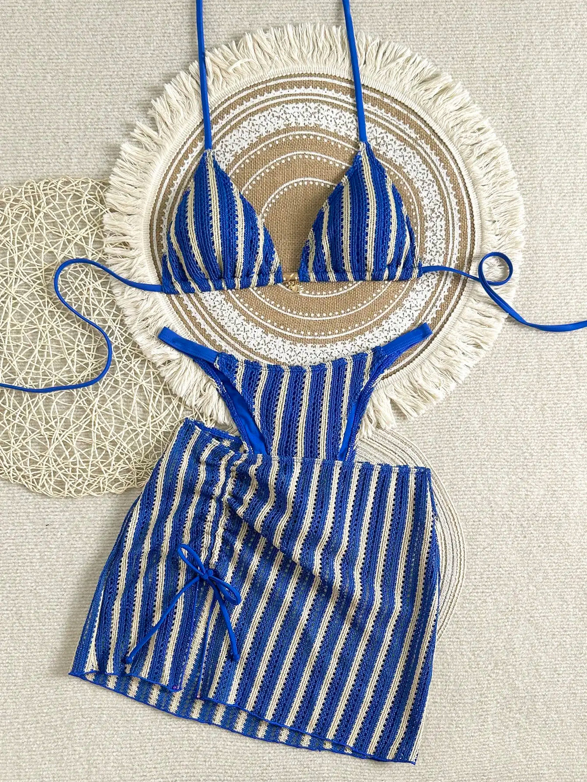 Flat lay of blue and beige striped knit bikini top, bottom and mini skirt cover up