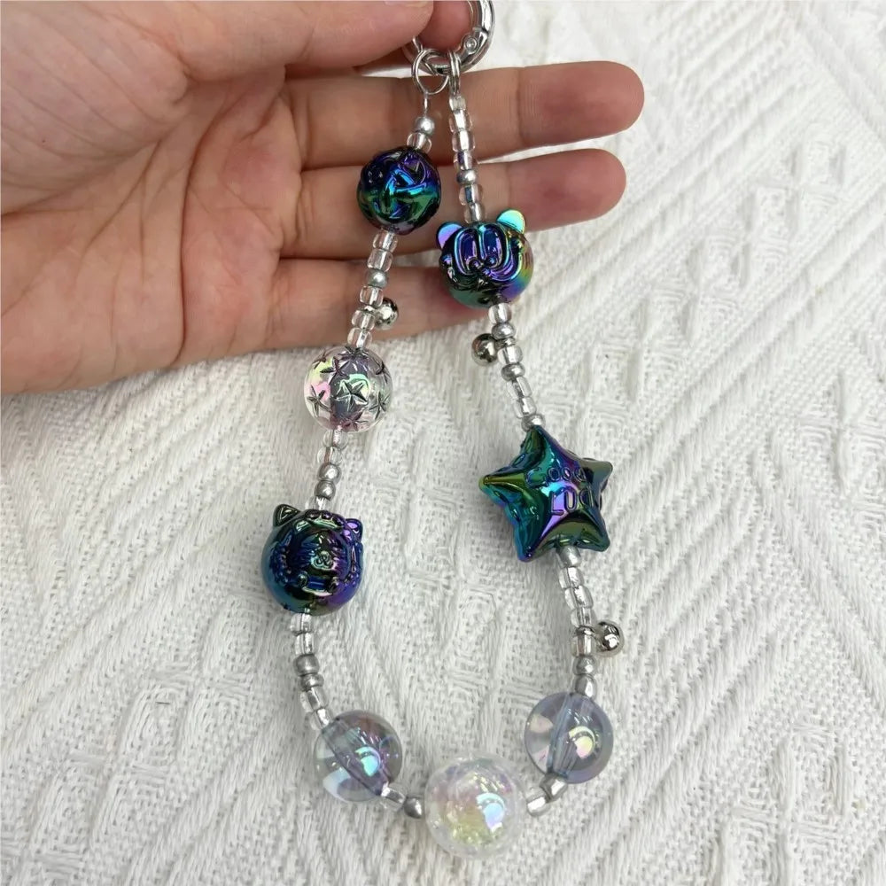 A hand holding an iridescent beaded lanyard or phone charm with star and bear shaped beads.