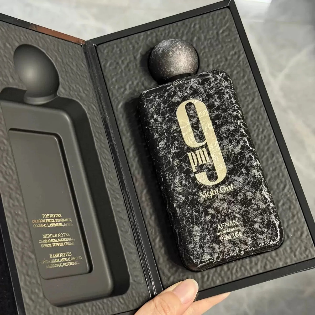 A black textured men's perfume bottle in an open presentation box showing fragrance notes.