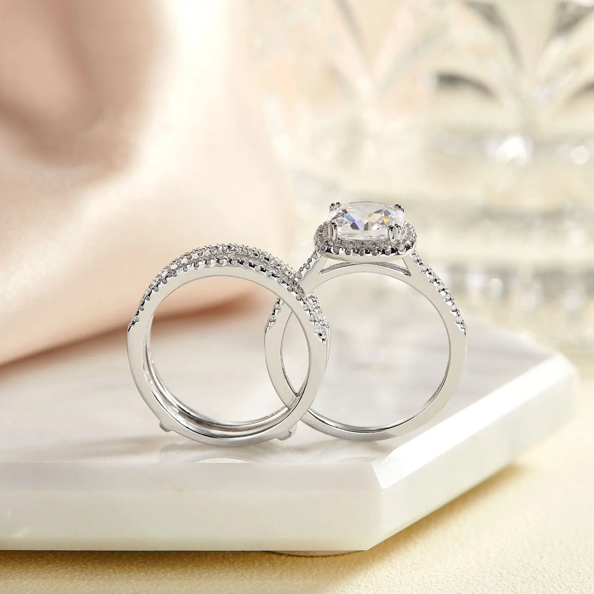 Cushion cut halo engagement ring stacked with two pave wedding bands on a marble surface