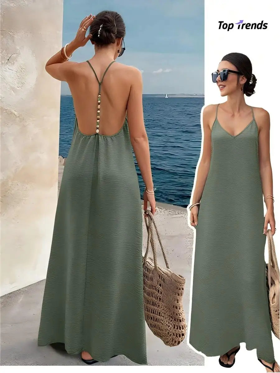 Woman wearing a khaki green backless maxi dress with thin straps and beaded detailing, paired with a straw bag