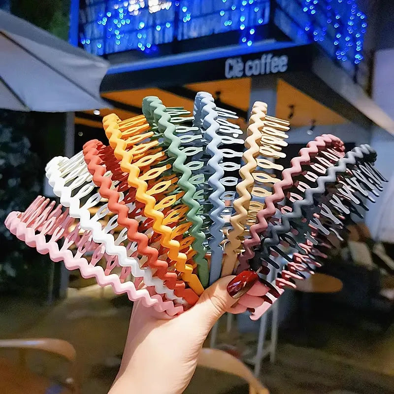 A hand holding a stack of wavy, colorful toothed plastic headbands