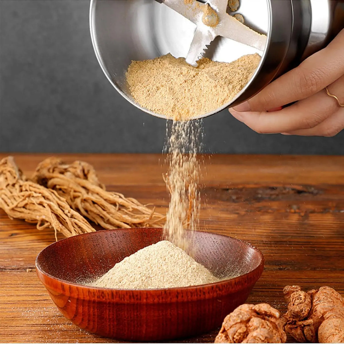 Close-up of stainless steel electric grinder pouring ground herbs into a wooden bowl
