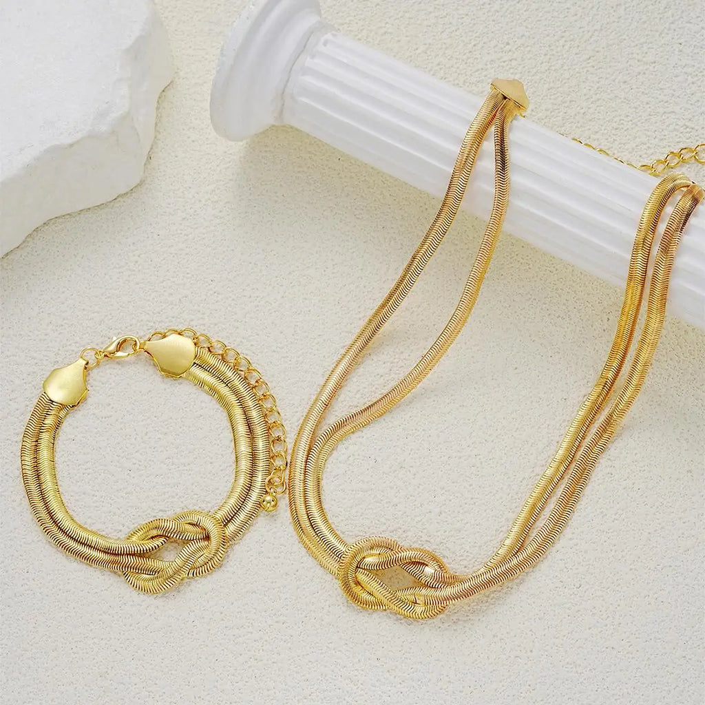 Gold double layer knot necklace and matching bracelet resting on a white cylindrical stand