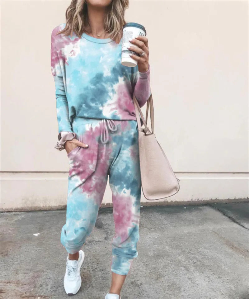 A woman wearing a blue and pink tie-dye long-sleeve top and jogger pants set, holding a takeaway coffee cup.