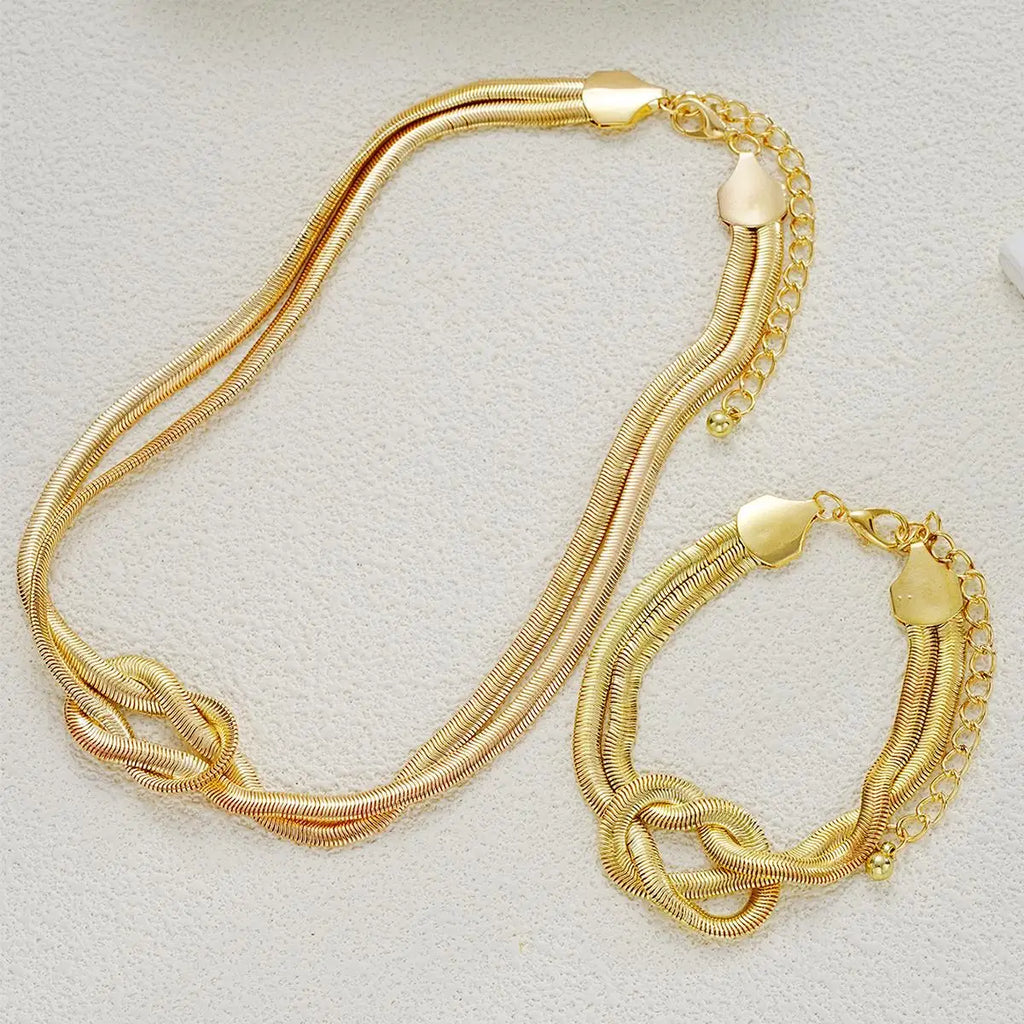 Gold double layer knot necklace and matching bracelet on a white textured surface