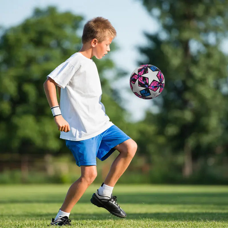 A young boy practicing football skills by kicking a patterned soccer ball on a field