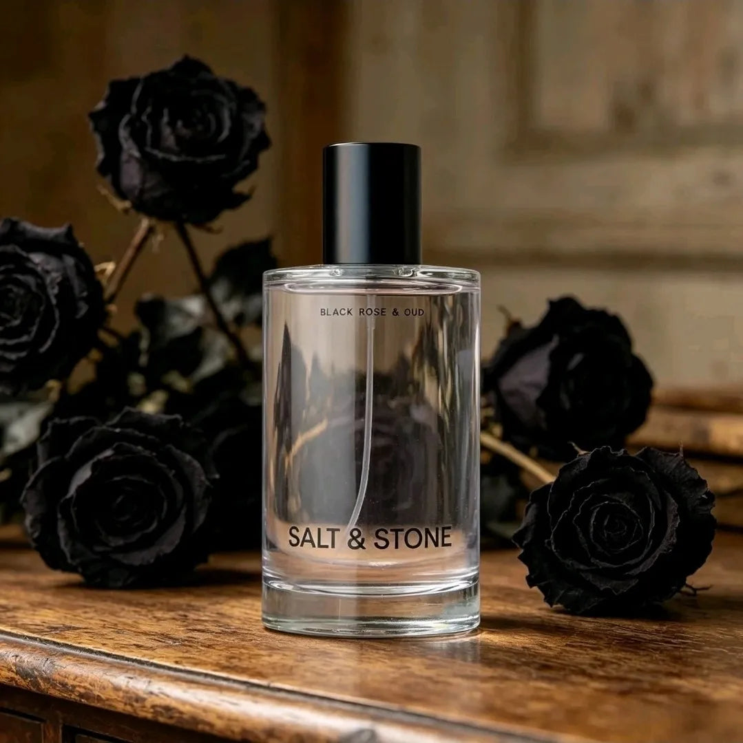 Body mist fragrance bottle displayed with black roses on a wooden surface