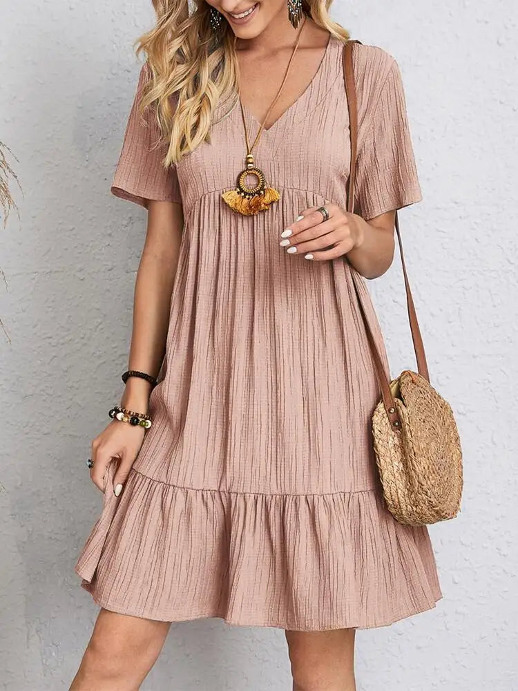 A woman wearing a short-sleeved light brown V-neck textured mini dress with a tiered ruffle hem and a round straw crossbody