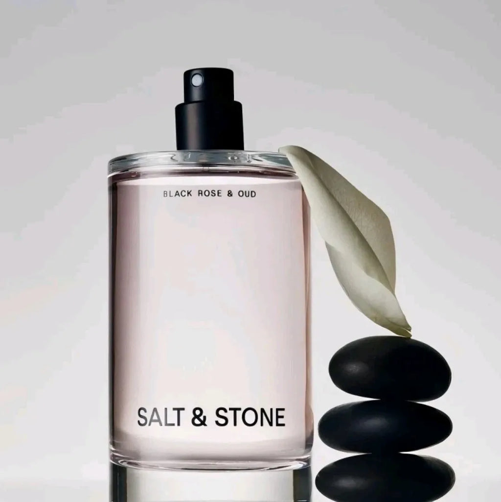 Body mist fragrance bottle next to a single white leaf and a stack of black stones