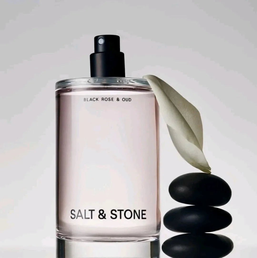 Body mist fragrance bottle next to a single white leaf and a stack of black stones