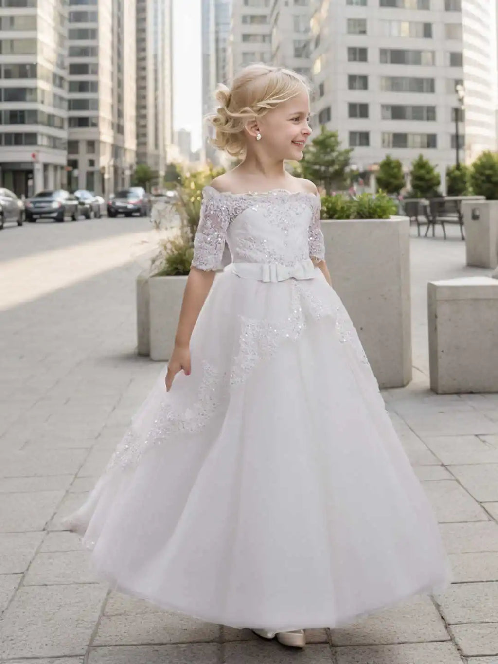 A girl wearing a white off-shoulder lace and sequin ball gown dress walking on a city sidewalk.