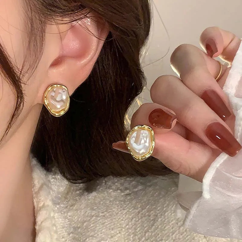 Person wearing gold-rimmed irregular pearl earrings