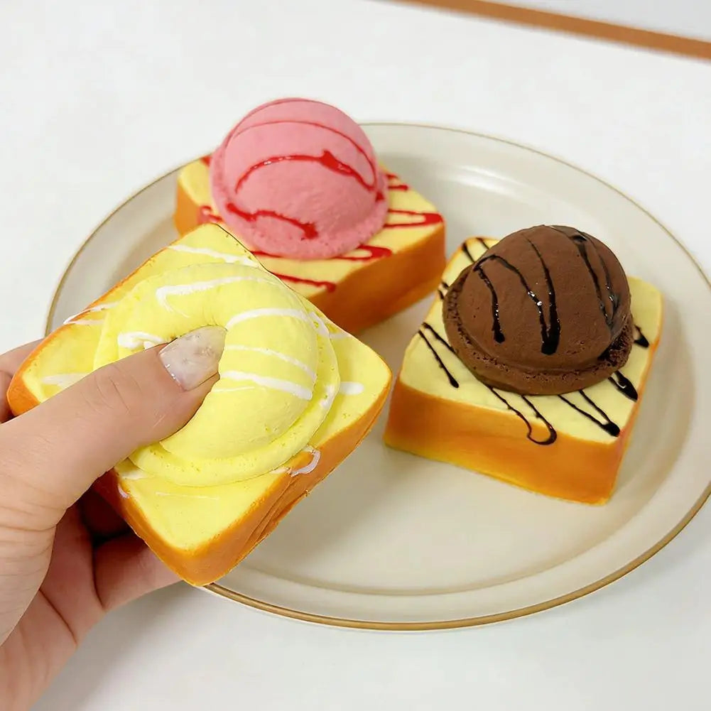 Hand holding a yellow ice cream bread squishy toy next to others on a plate